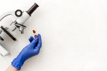 Research with microscope, hands hold blood sample. White table top view copy space