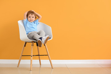 Cute little boy sitting on chair near color wall