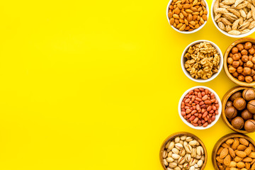 Set of macadamia, hazelnut, walnut, almond, pistachio, pecans nuts on yellow background top-down frame copy space