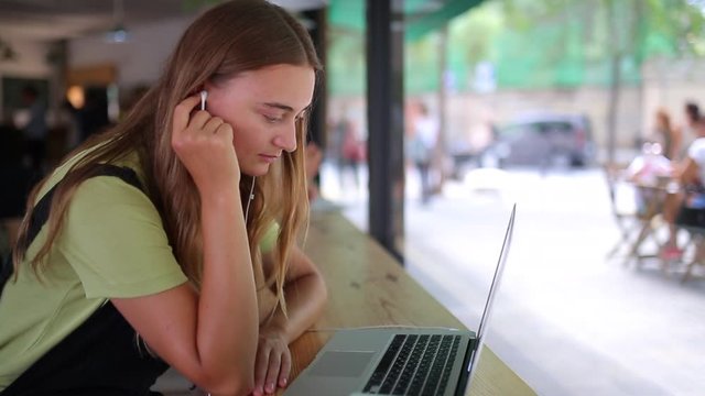 Young caucasian student female listening with attention online lesson wearing headphones. Freelance woman enjoys public workspace, study online e-learning, checking e-mail, news feed or works
