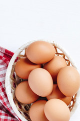 Brown chicken eggs in a straw basket on white wooden background. Top view with copy space.