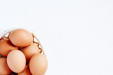 Brown chicken eggs in a straw basket on white wooden background. Top view with copy space.