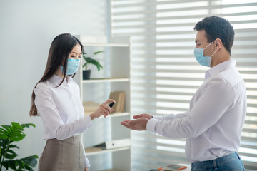 Fototapeta premium Dark-hired woman holding a sanitizer and spraying it on mans hand