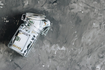 One hundred dollar banknotes in a glass bank on a gray concrete background. Top view with copy space. - 341204128
