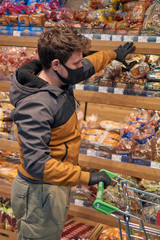 Man in disposable medical face mask and gloves buying in supermarket. Panic shopping during Coronavirus covid-19 pandemic.