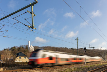 On a railway line on the German island of Rügen in the Baltic Sea. A regional train passes quickly. In the background the white castle of Lietzow on a mountain. Blue sky and clouds.