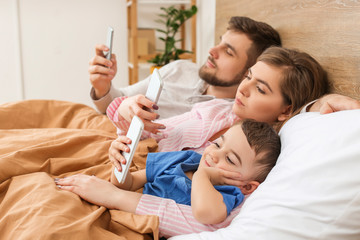 Obraz na płótnie Canvas Happy family with mobile phones in bedroom