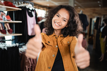 beautiful young asian fashion shop owner at her boutique standing proudly and showing thumb up