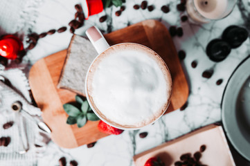 Elegant coffee break the view from the top. A full Cup of milk froth on a marble table with a Turkish coffee pot, scattered coffee beans, coffee capsules, strawberries, and candles.
