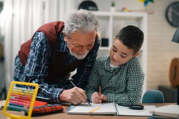 Grandfather and grandson working homework together. Grandpa and grandson enjoying at home.