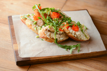 Italian bruschetta with salmon butter, capelin caviar, cherry tomatoes and parsley served on wooden cutting board
