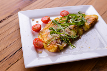Omelette with vegetables served on a square white plate over dark rustic wooden table background.