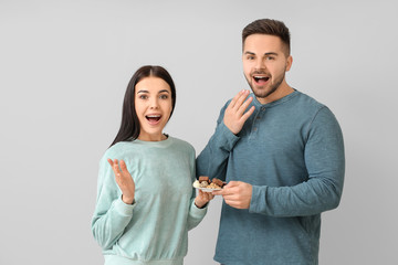 Surprised young couple with tasty chocolate on light background