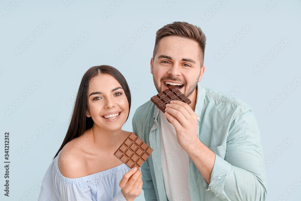 Wall mural Beautiful young couple with tasty chocolate on light background