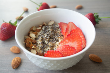 Healthy vegan oatmeal porridge with strawberries, chia seeds and sliced almonds in a white bowl with strawberries and whole almonds in the background