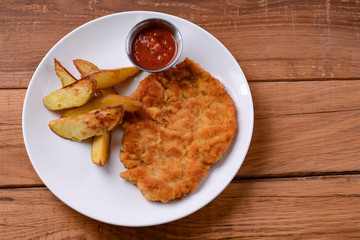 Juicy steak meat with tomato sauce and french fries served on white plate over dark rustic wooden...