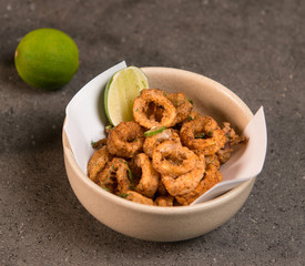 Deep fried calamari rings and lime in a white bowl with on a table