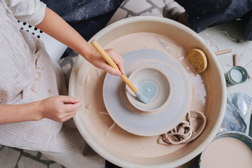Girl hands painting clay bowl on a pottery wheel in a private workshop - obrazy, fototapety, plakaty