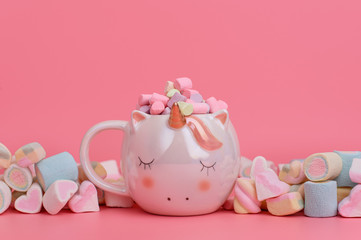 Unicorn mug with colourful marshmallows on a pink background. Sweets concept with place for text. Copy space on vivid pink background.