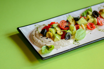 Fresh vegetables and green salad with sauce served on traditional rectangular white plate over bright green background.