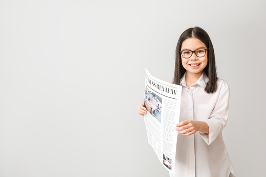 Cute little businesswoman with newspaper on grey background