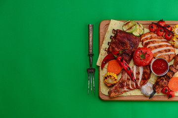 Top view of grilled meal of steak and vegetables spread out on rustic wooden board over bright green background