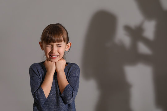 Afraid little girl and shadow of her quarreling parents on grey background