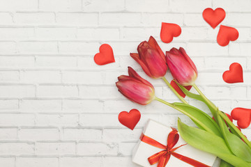 Red Flowers tulips, hearts and gift box with red bow on a white background of wall of brick, spring and holidays, Women's Day.