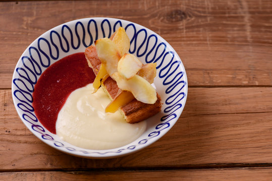 Sweet fruit dessert with delicious gruit and milk sauce served in a white bowl over rustic wooden table background.