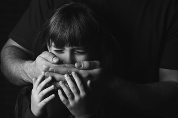 Father covering mouth of his scared little daughter on dark background. Concept of domestic violence