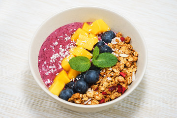 Handmade Bowl healthy tasty breakfast of yogurt, smoothie with granola, nuts, mango and berries.