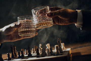 Close up of hands of men playing chess and drinking whisky.	

