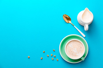 Cup of tasty cappuccino and jug of milk on color background