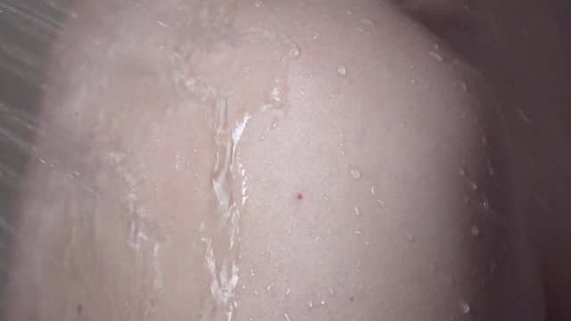 Water jets from a shower fall on a female shoulder. Close-up