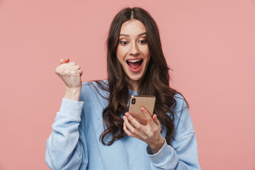 Image of excited young woman making winner gesture and using cellphone