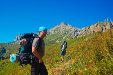 Tourists with backpacks hike on mountain under blue sky