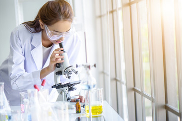 Attractive young Asian scientist woman lab technician assistant analyzing sample in test tube with microscope at laboratory. Medical, pharmaceutical and scientific research and development concept.