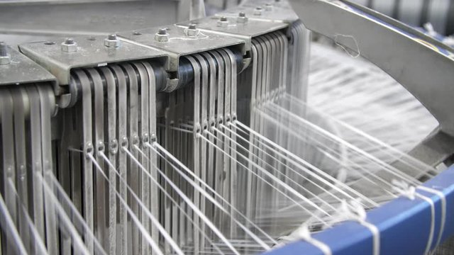 Techno closeup of knitting metallic device with rushing back and forth plastic strings producing plastic tissue for agricultural sacks at contemporary workshop