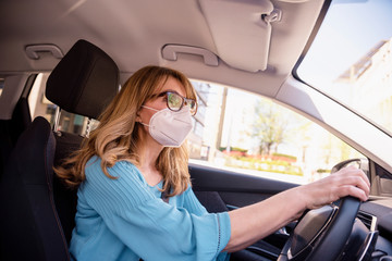 Mature woman wearing face mask while driving her car during coronavirus pandemic