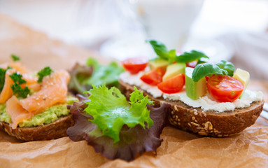 Wholegrain toast with avocado, tomato and salmon on wooden cutting board
