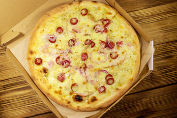 Delicious fresh pizza in cardboard box on a wooden table. Top view. Concept for home delivery of food, fast food, delivery of pizza