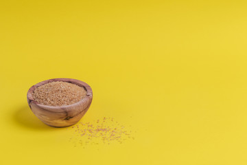 Brown sugar heap in bowl on yellow background
