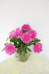 glass vase with pink fresh picked paeony flowers on a round table with butterfly tablecloth vertical