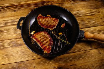 Grilled pork steaks with rosemary, garlic and spices in cast iron grill frying pan on wooden table....