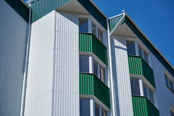 facade of a new multistory building with white and green metal siding, many Windows