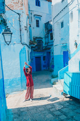 Fototapeta na wymiar raising hands up a girl in oriental clothes stretches on the streets of the blue city of morocco