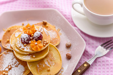 pancakes with maple syrup, raspberries, powdered sugar and physalis in pink plate with cup of coffee for Breakfast