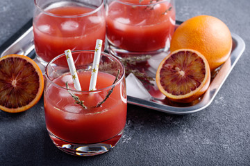 closeup freshly squeezed juice from red oranges in glasses with tubes and with ice cubes on gray background