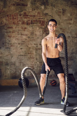 Young athlete man in training with ropes against background of brick wall