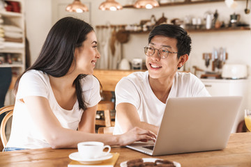 Image of happy couple smiling and using laptop while sitting at table